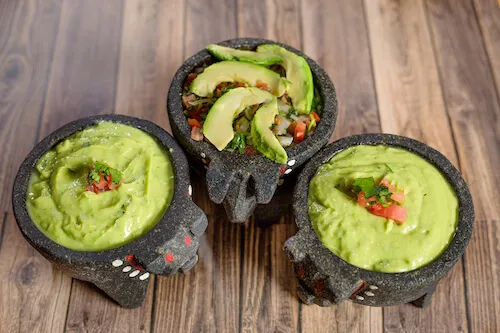 Three molcajete bowls of guacamole, two topped with sliced avocado