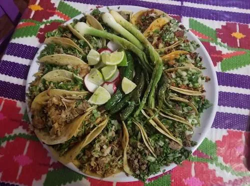 Tray of tacos with green onions and lime wedges on a colorful woven cloth
