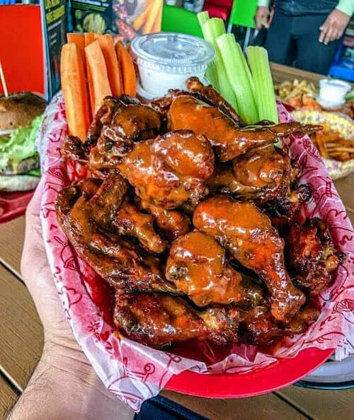 Basket of buffalo wings with carrot and celery sticks, held in one hand