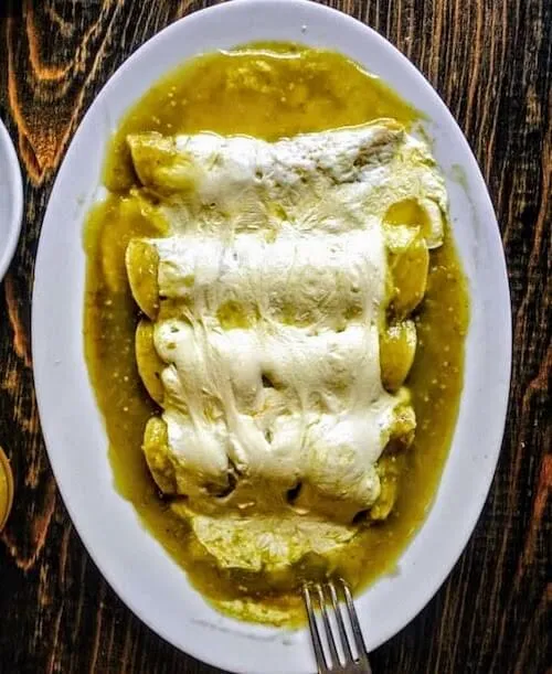 Enchiladas covered in green sauce and melted cheese on an oval plate