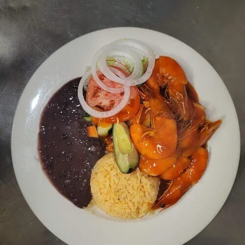 Shrimp in orange sauce with sliced onion, black beans and rice on a white plate