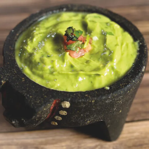 Guacamole in a black stone molcajete on a wooden tabletop