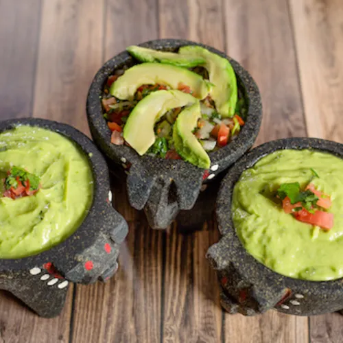 Three molcajete bowls of guacamole, two topped with sliced avocado