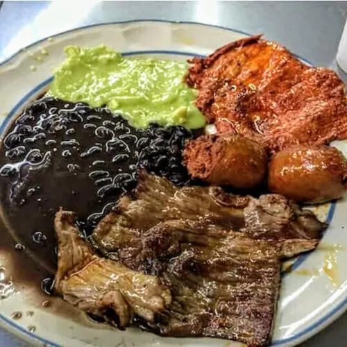 Black beans, guacamole and thin-cut grilled beef on a blue-rimmed plate