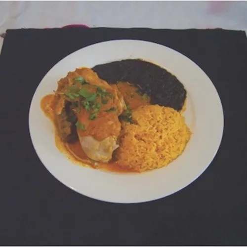 Piece of meat in orange sauce with cilantro, rice and black beans on a black placemat