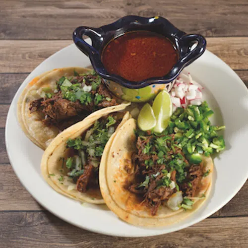 Three tacos with lime and cilantro beside a small bowl of red salsa