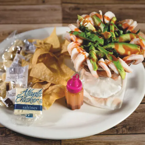 Shrimp plate with cucumber and avocado beside tortilla chips on a wooden tabletop