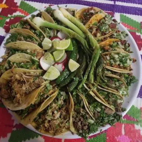 Tray of tacos with green onions and lime wedges on a colorful woven cloth