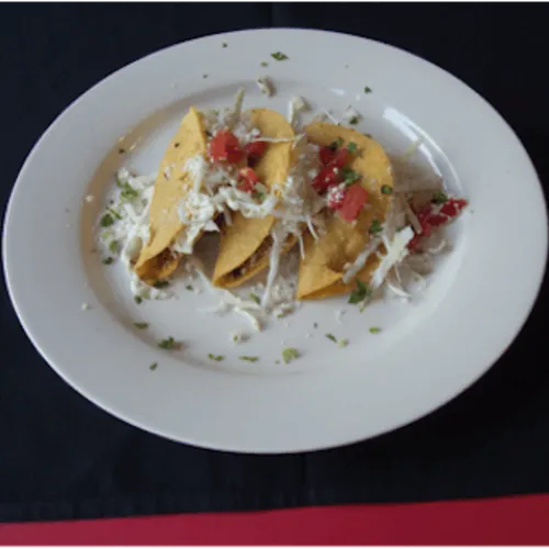 Three small fried tacos topped with cheese and salsa on a white plate
