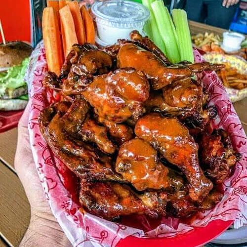 Basket of buffalo wings with carrot and celery sticks, held in one hand
