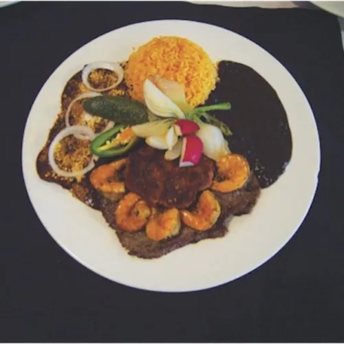 Steak topped with grilled shrimp, with rice and black beans on a black placemat