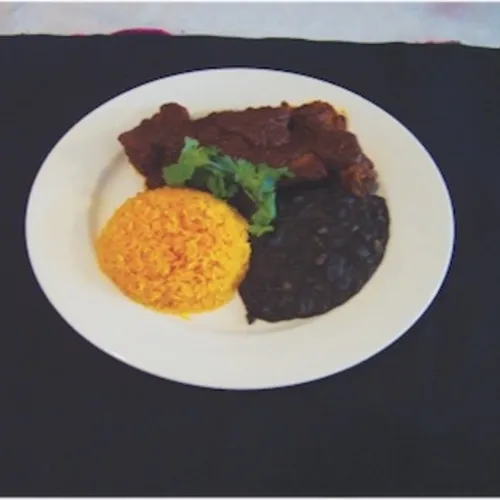 Stewed meat in dark sauce with rice and black beans on a black placemat