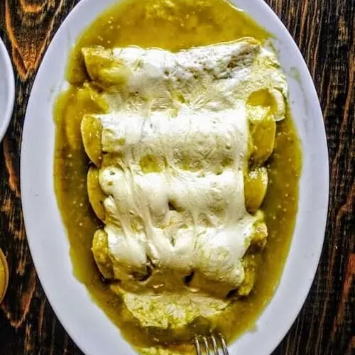 Enchiladas covered in green sauce and melted cheese on an oval plate