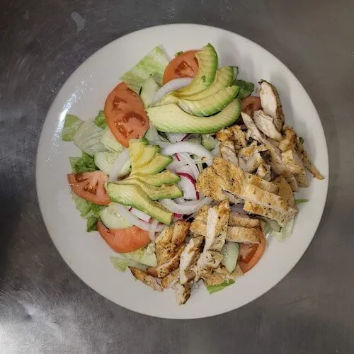 Salad with grilled chicken, avocado and tomato on a white plate