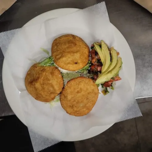 Three fried corn cakes beside avocado and pico de gallo on parchment